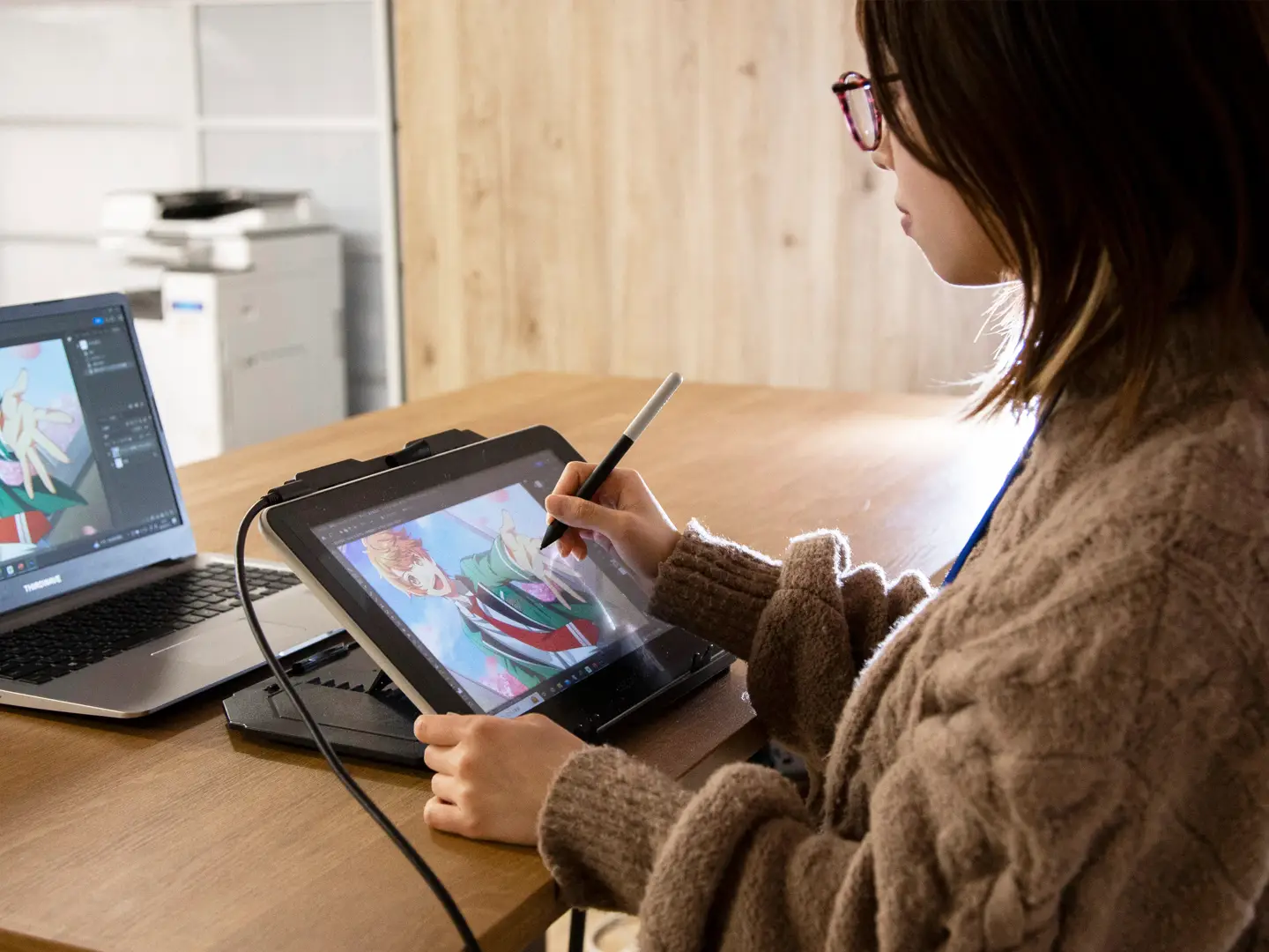 写真：ノートPCにタブレットを繋いでイラストを描いている女性社員